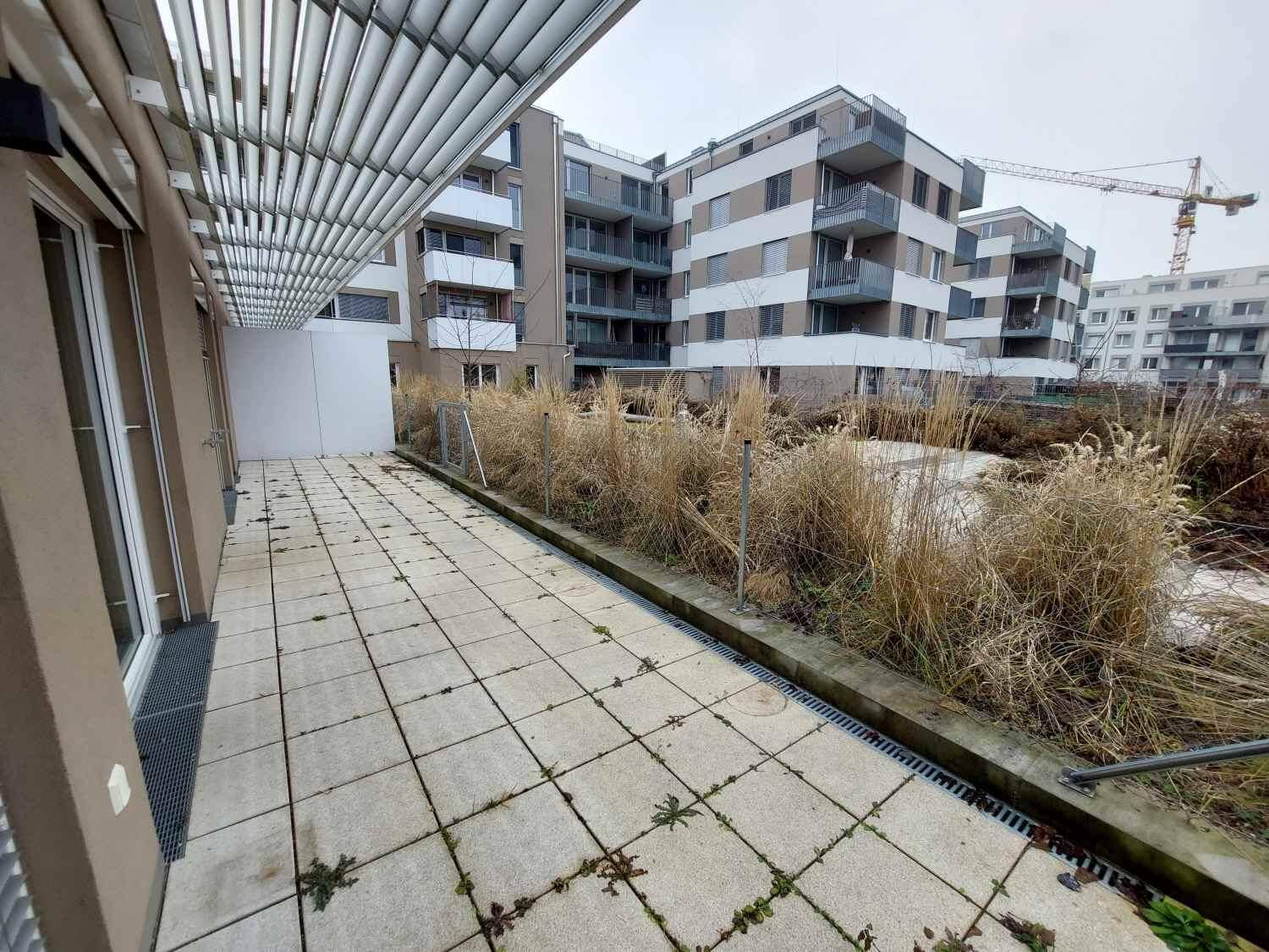Geräumige Terrasse mit Plattenboden und Blick auf moderne Wohngebäude sowie Baustellenkräne in der Ferne.