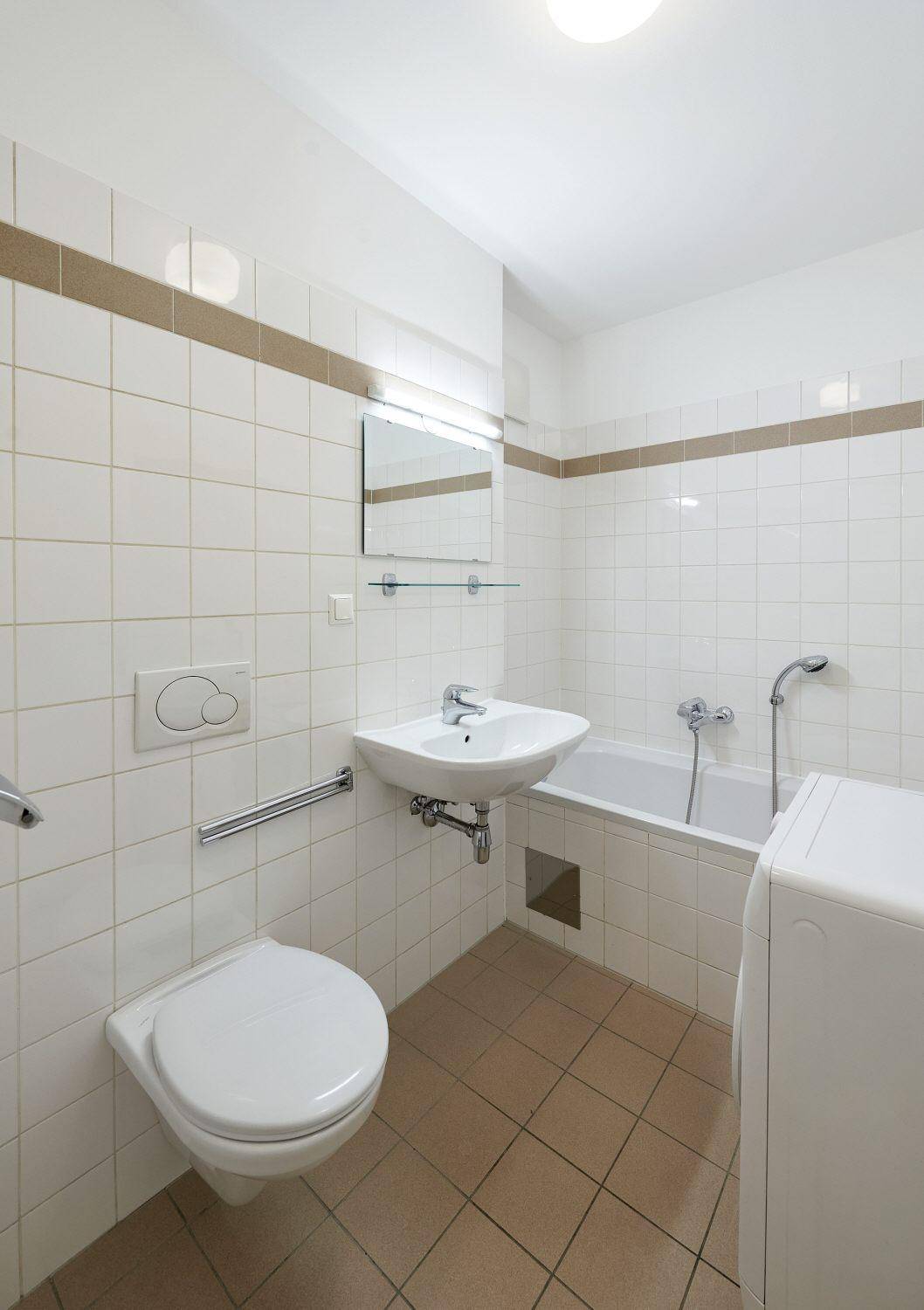 Sauberes Badezimmer mit Badewanne, WC, Waschbecken und Waschmaschine, ausgestattet mit hellen Fliesen.