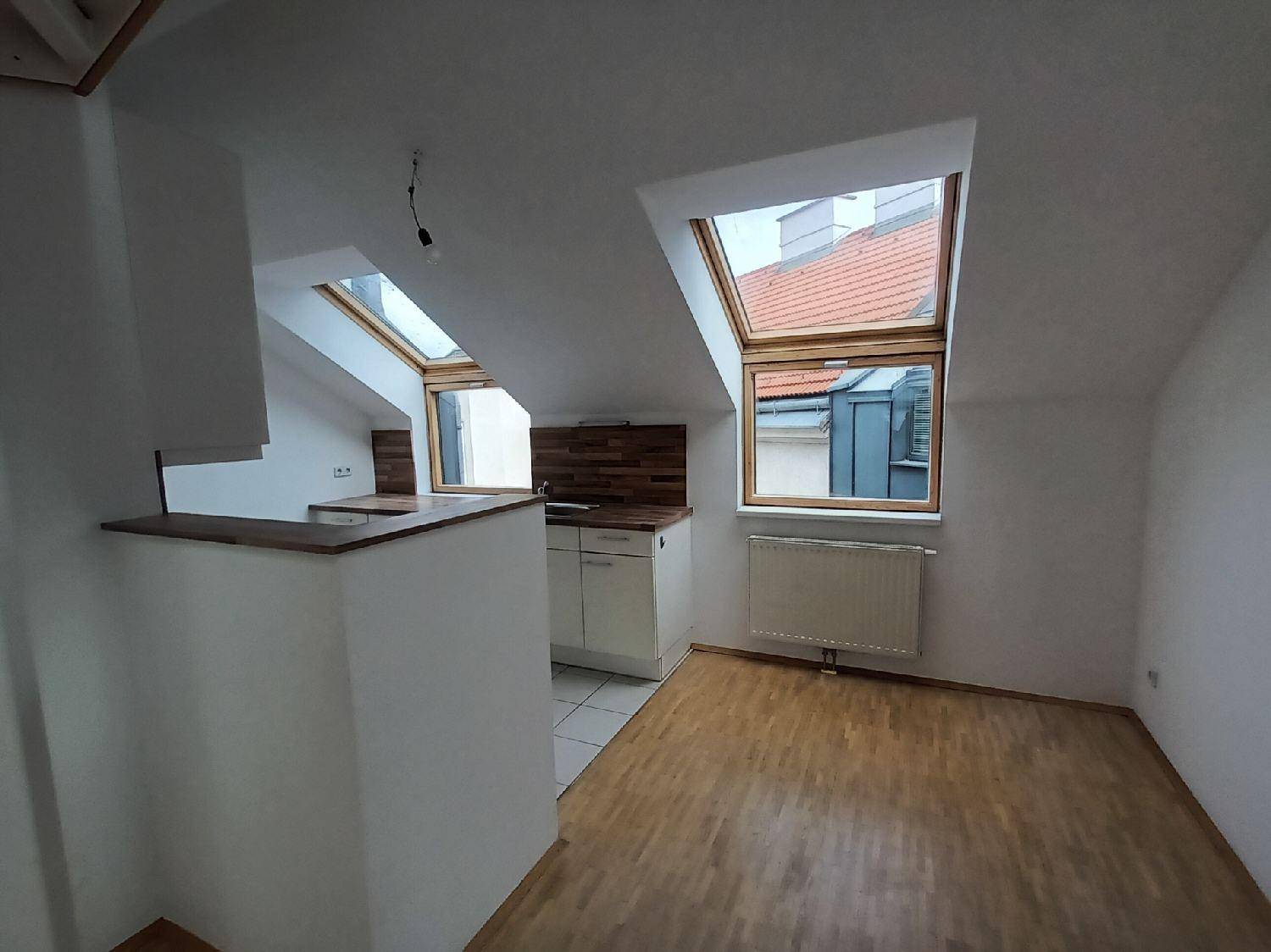 Helle Küche im Dachgeschoss mit Dachfenstern, Holzarbeitsplatten und Fliesenboden unter schräger Decke.