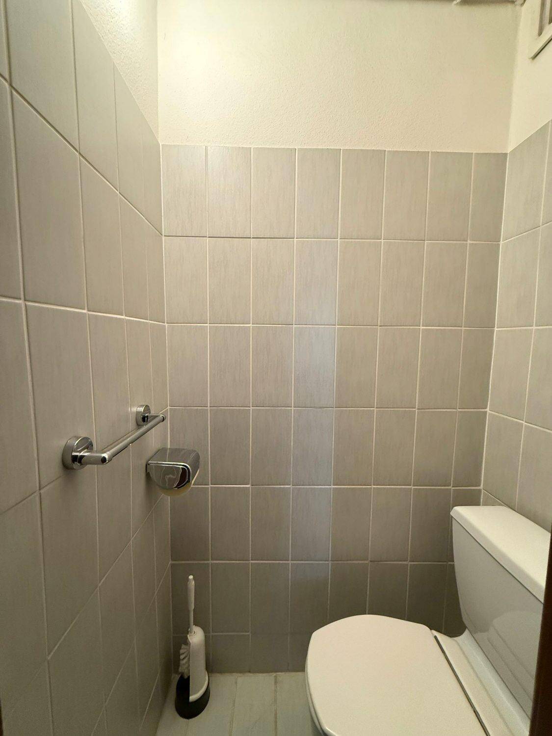 Kleines WC mit Toilette und hellgrauen Fliesen an den Wänden.
