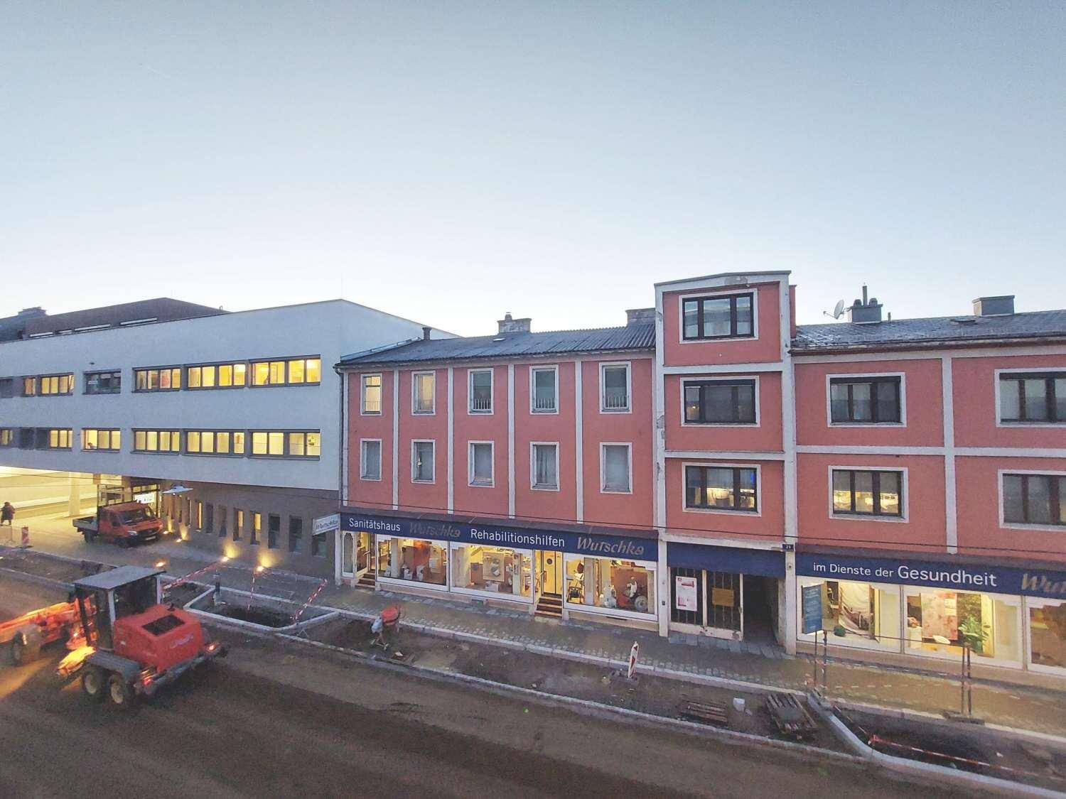 Stadtansicht mit Geschäftsgebäuden und einer Baustelle im Vordergrund bei Dämmerung.
