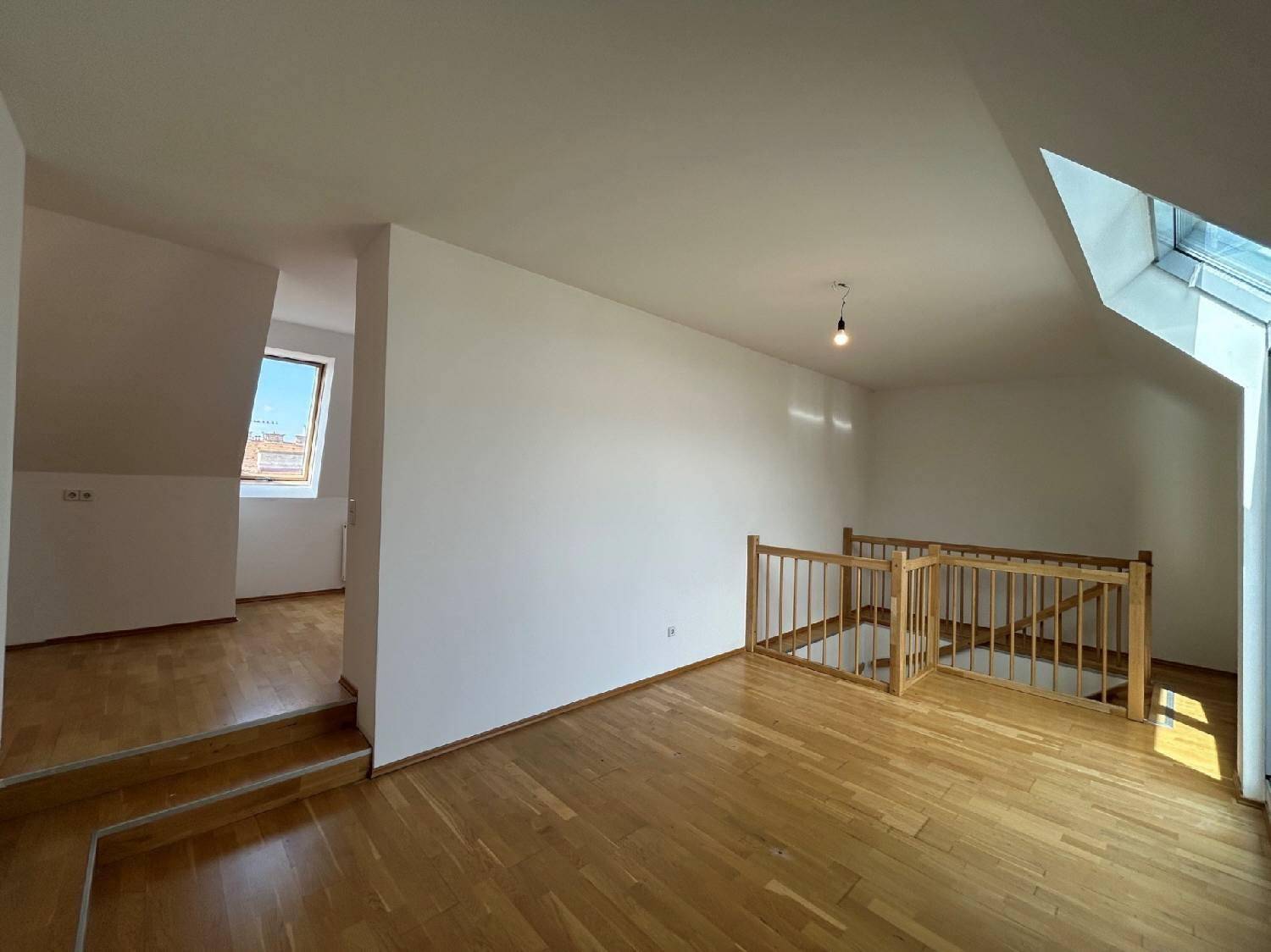 Heller Wohnbereich im Dachgeschoss mit Holzparkettboden und offener Treppe zu einer weiteren Ebene.