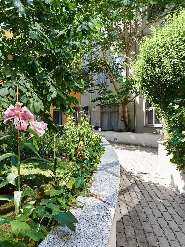 Detailansicht eines grünen Innenhofs mit blühenden Lilien und einem gepflasterten Weg.