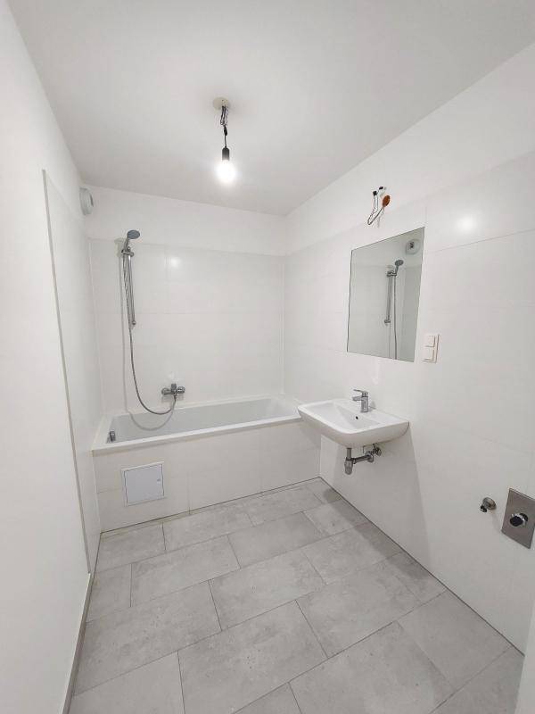 Modernes Badezimmer mit weißen Fliesen, Badewanne mit Duschfunktion und einem Waschbecken.