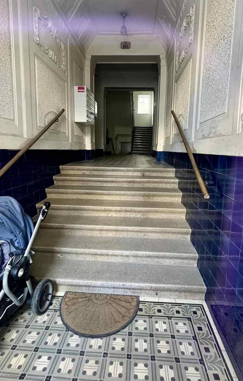Heller Eingangsbereich eines Altbaus mit gemusterten Fliesen, Treppe und blauen Wandfliesen.