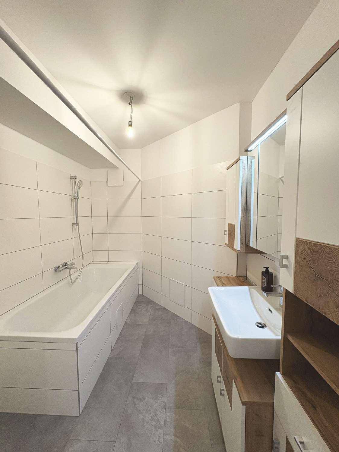 Modernes Badezimmer mit Badewanne, Waschbecken und Spiegelschrank, hell gefliest.