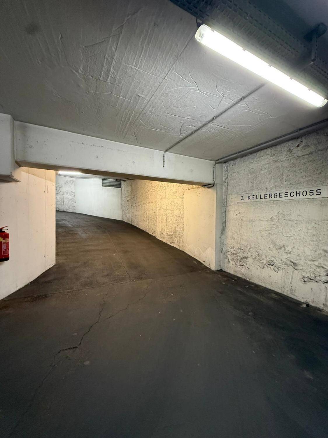 Abfahrt zum zweiten Kellergeschoss einer Tiefgarage mit Betonwänden und Beleuchtung.