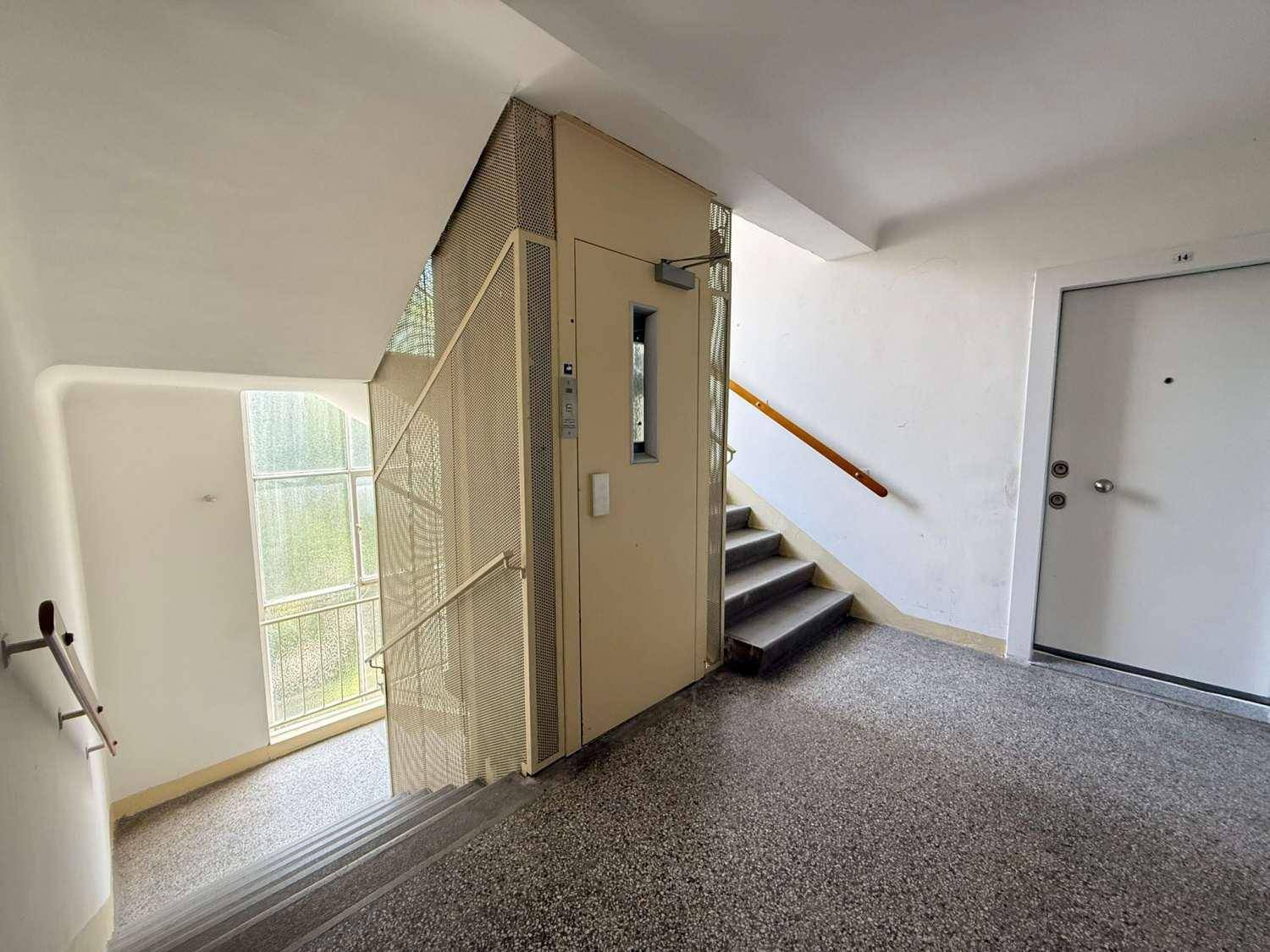 Treppenhaus und Aufzug in einem Mehrfamilienhaus, mit Terrazzoboden und Handläufen.