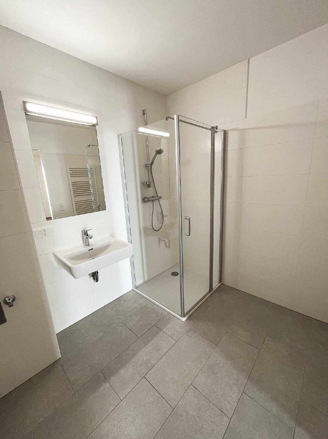 Modernes Badezimmer mit Duschkabine, Waschbecken und hellen Fliesen an Wänden und Boden.