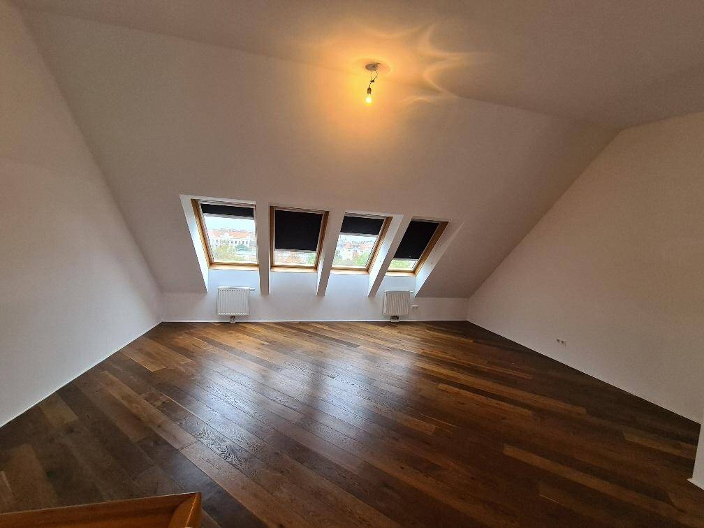 Helles Dachzimmer mit schrägen Wänden, Holzboden und mehreren Dachfenstern für viel Tageslicht.