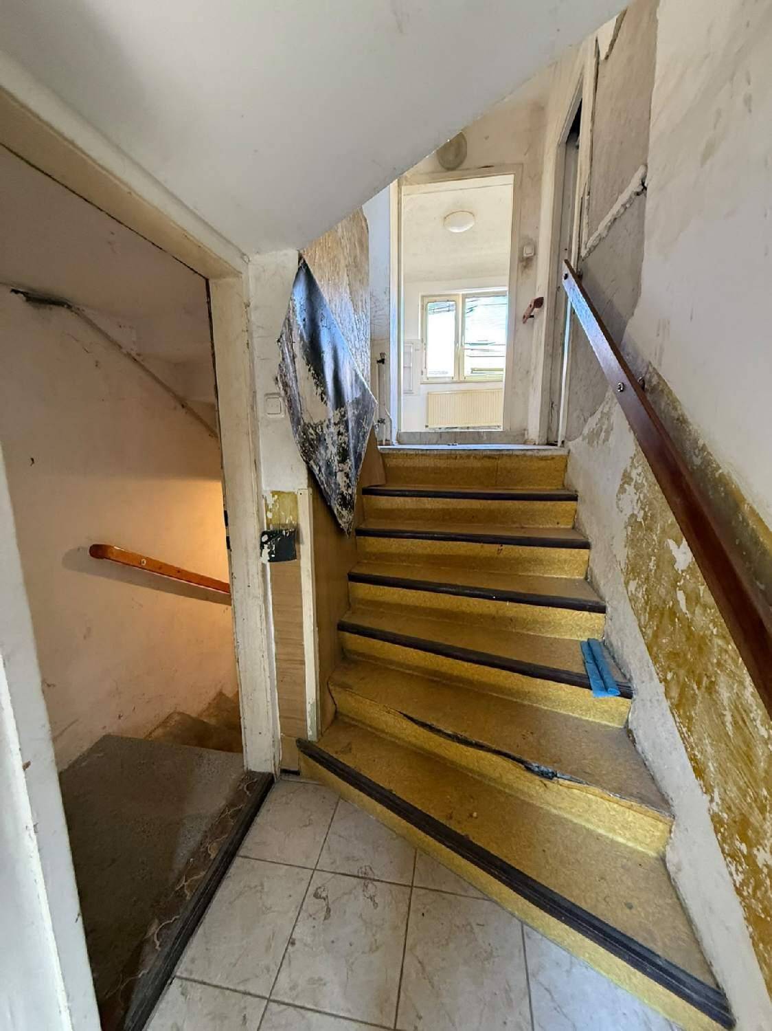 Treppenhaus mit Holztreppe und Fliesenboden, das in die oberen Stockwerke führt.