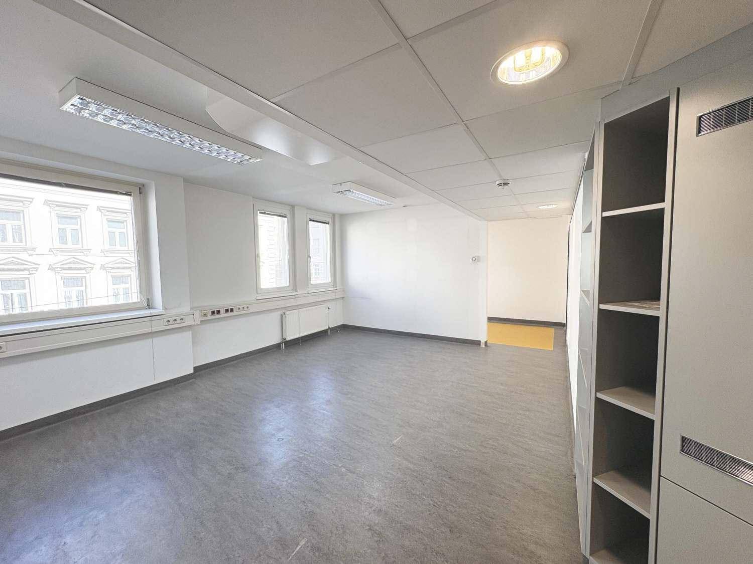 Leeres Büro mit grauem Linoleumboden, weißen Wänden und praktischen Einbauschränken entlang der Wand.