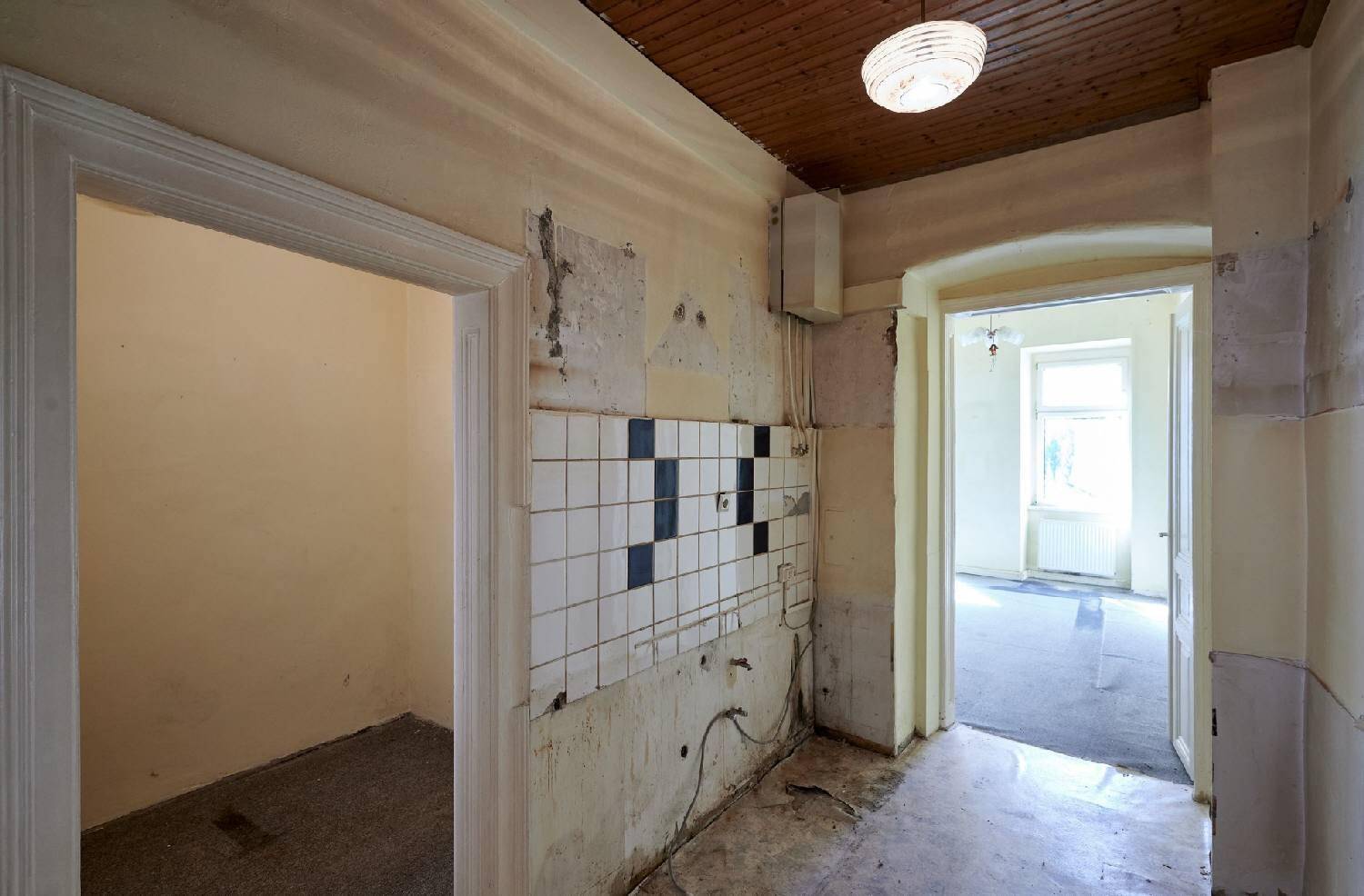 Flur mit sichtbaren Renovierungsspuren, Holzdecke und teilweise entfernten Wandfliesen.