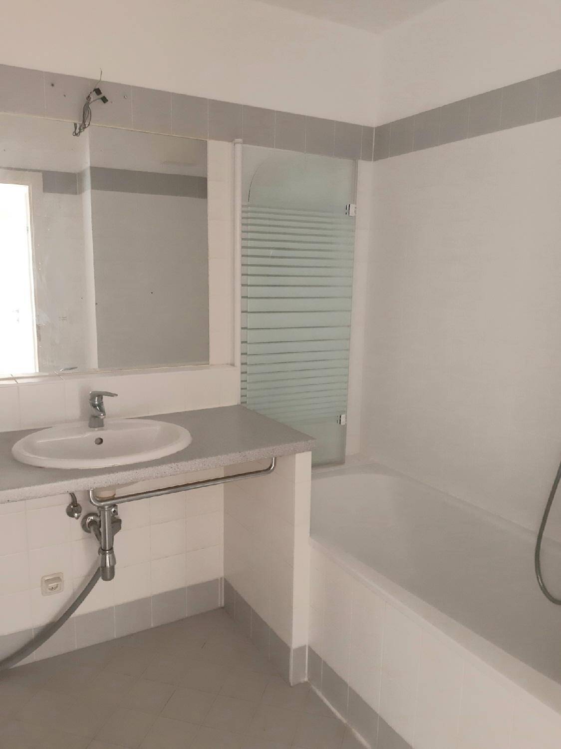 Badezimmer mit Badewanne, Duschwand, Einzelwaschbecken und hellgrauen Fliesen.