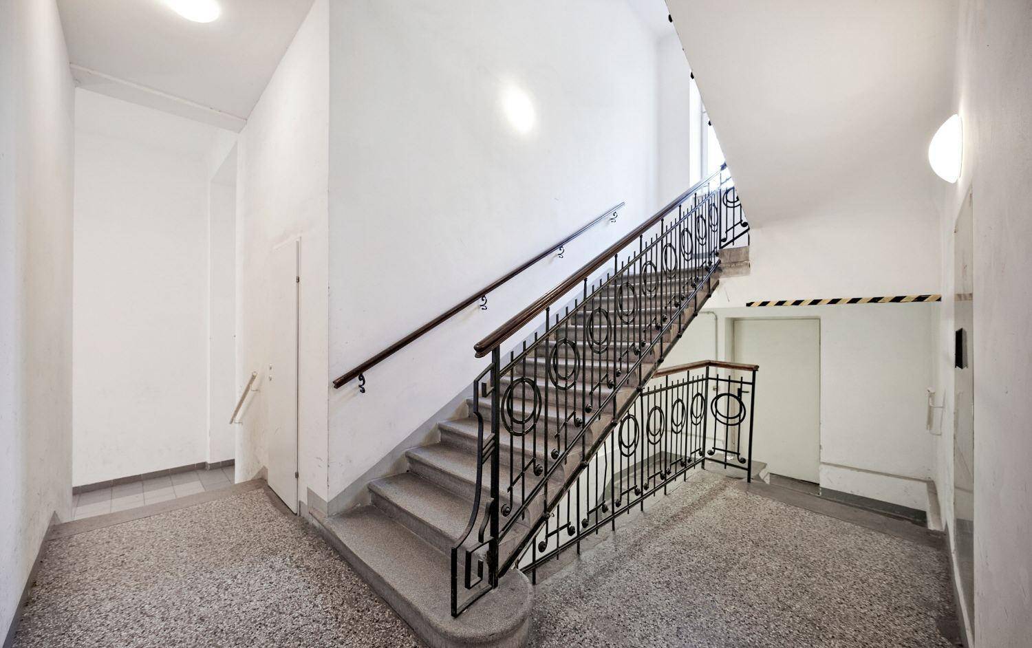 Treppenhaus mit klassischem schmiedeeisernem Geländer und Terrazzoboden in einem Mehrfamilienhaus.
