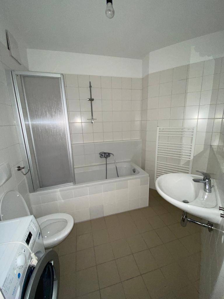 Gefliestes Badezimmer mit Badewanne, Duschabtrennung, Waschbecken und beheiztem Handtuchhalter.