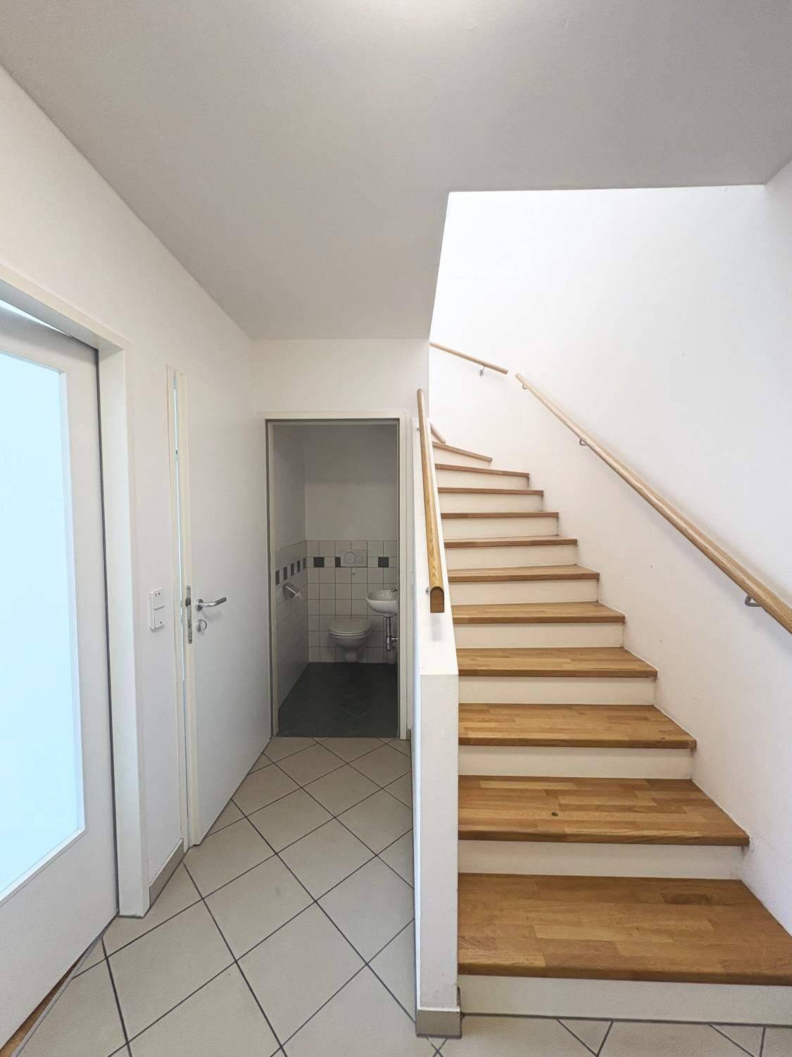 Heller Flur mit Fliesenboden, Holztreppe und integriertem Gäste-WC unter der Treppe.
