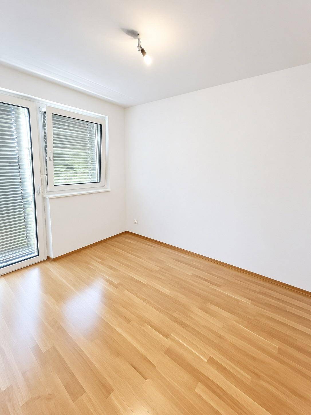 Helles Zimmer mit Parkettboden und großem Fenster, ideal als Schlafzimmer oder Büro.