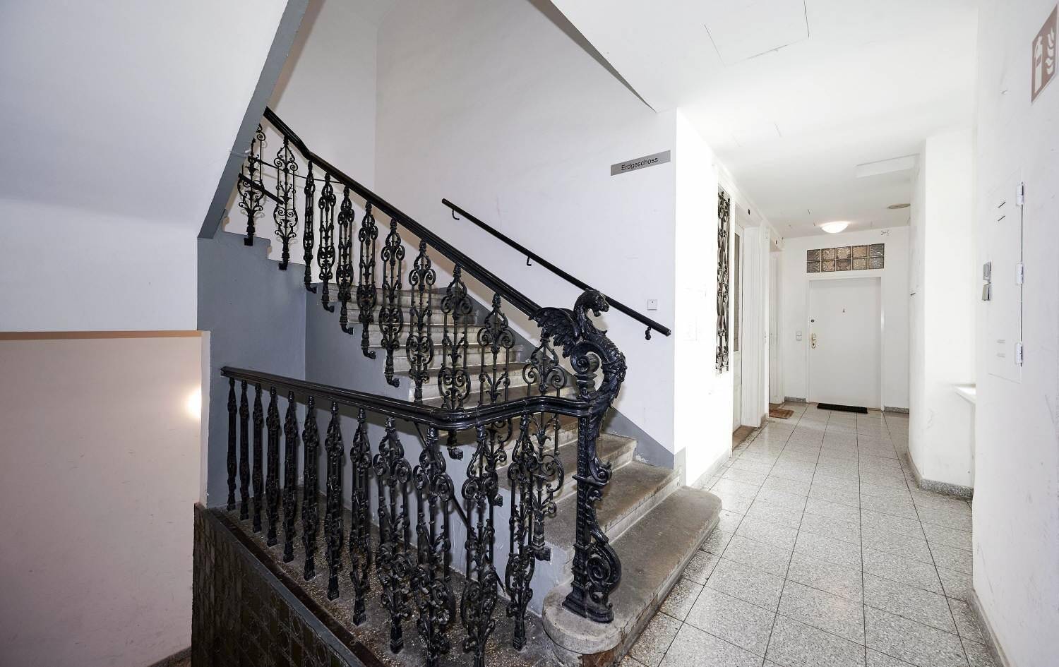 Historisches Treppenhaus mit schmiedeeisernem Geländer und Fliesenboden im Altbau.