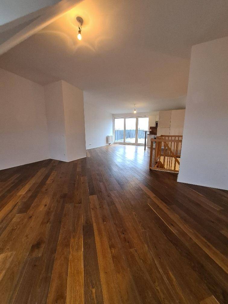 Geräumiger Wohnbereich mit glänzendem Holzboden und großen Fenstern, die auf die Terrasse führen.