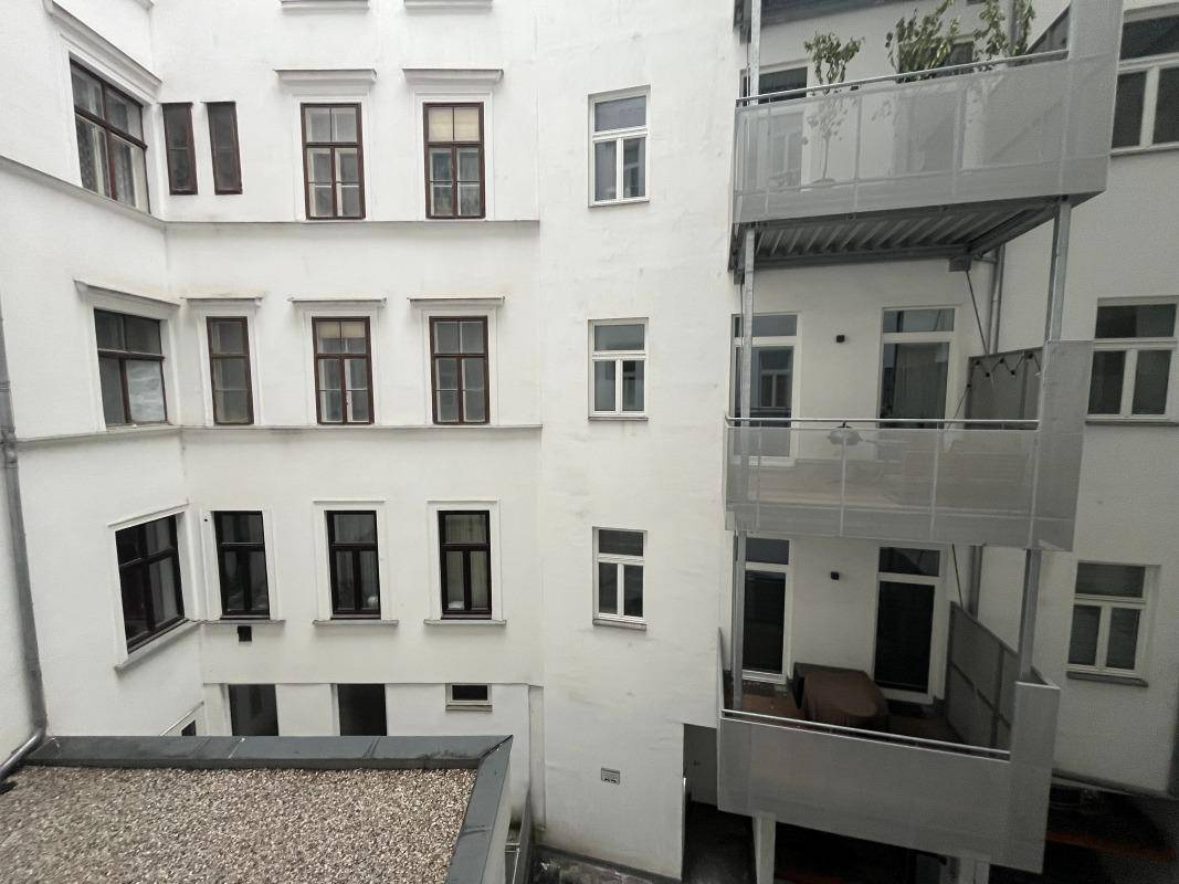 Blick in einen hellen Innenhof eines Wohngebäudes mit mehreren Balkonen und Fenstern.
