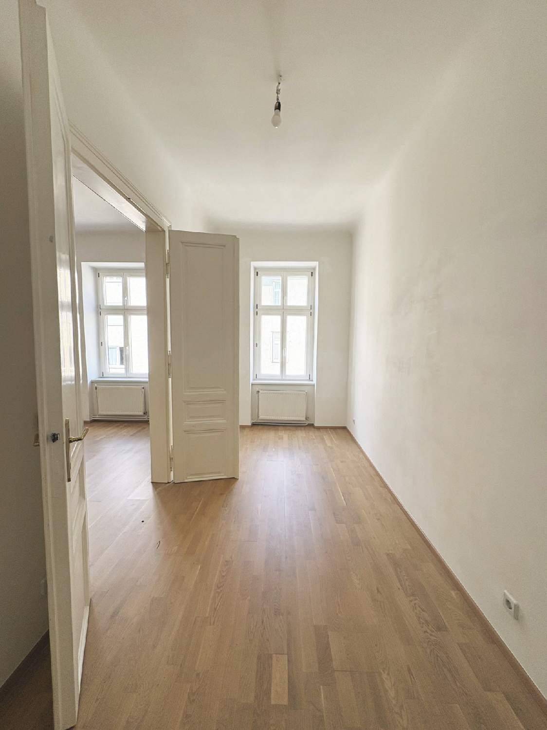 Lichtdurchflutetes Schlafzimmer mit hellem Parkett und zwei Fenstern, bietet viel Tageslicht.