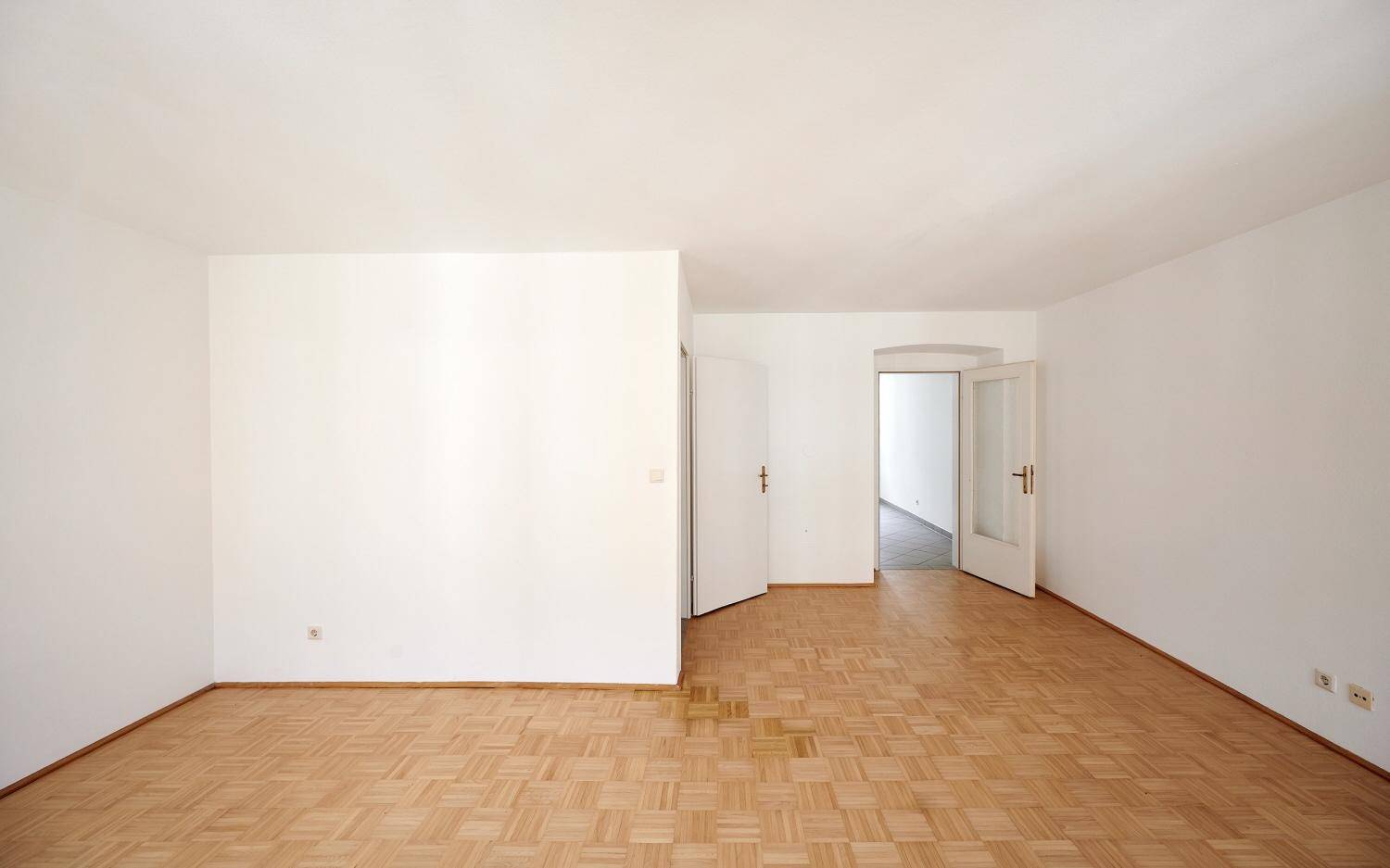 Geräumiges, helles Zimmer mit Parkettboden und Zugang zu weiteren Räumen, ideal für offenes Wohnen.