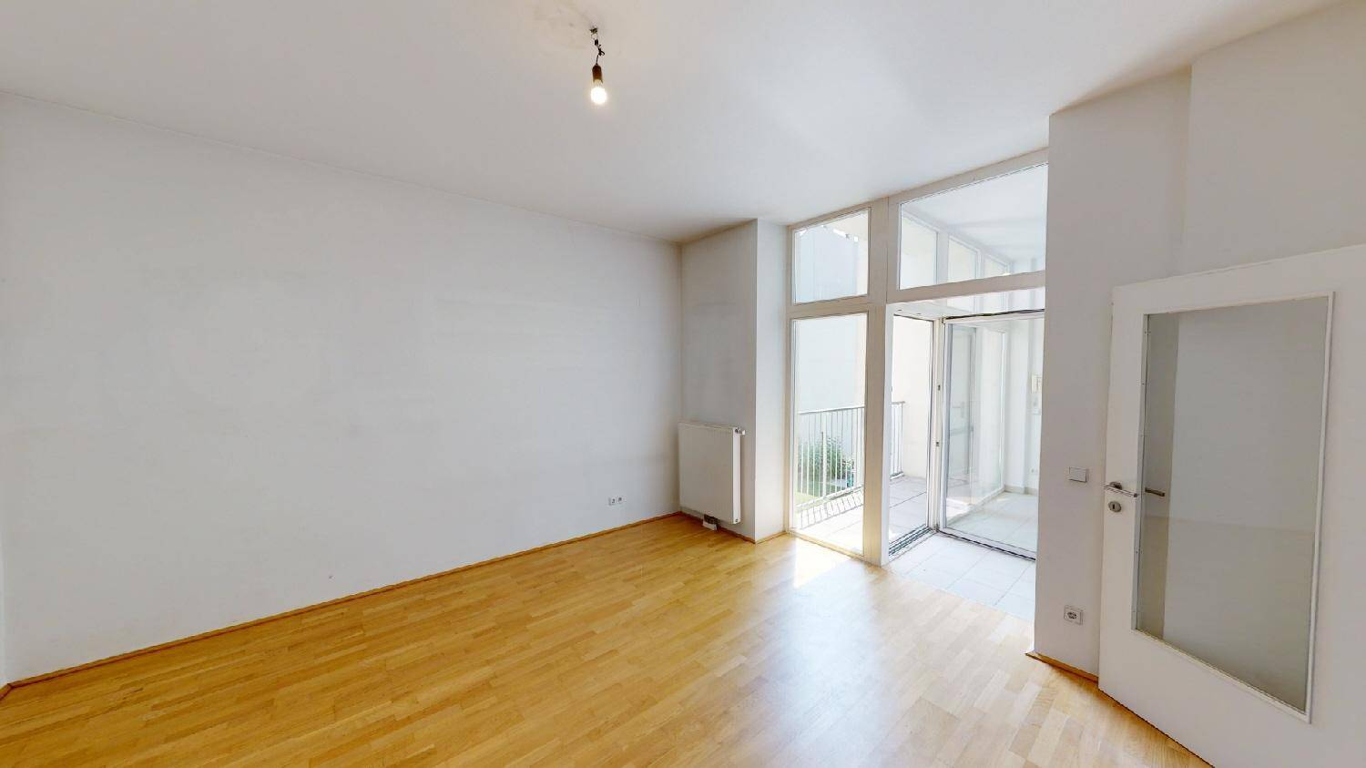 Geräumiges, helles Wohnzimmer mit Holzboden und großen Fenstern zum Balkon.