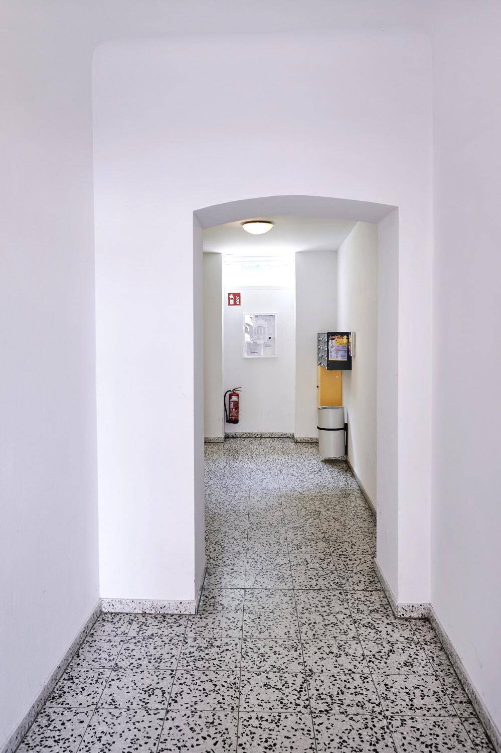 Heller Gemeinschaftsflur mit gefliestem Boden und Durchgang zu weiteren Bereichen.