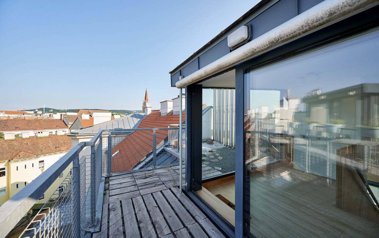 Dachterrasse mit Holzbelag, Metallgeländer und weitem Blick über die Dächer der Stadt.