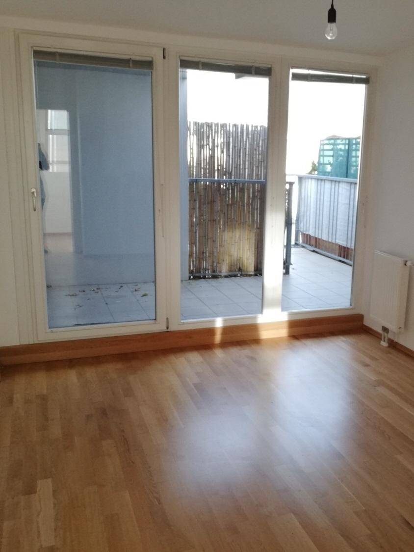 Heller Raum mit Holzboden und Zugang zu einem gefliesten Außenbereich mit Bambus-Sichtschutz.