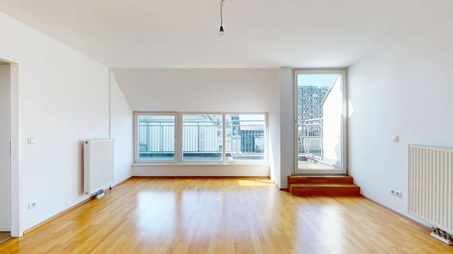 Heller Wohnraum mit Holzboden und Zugang zu einem Balkon oder einer Terrasse.