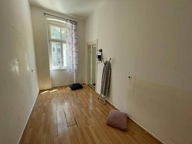 Schmaler Raum mit Laminatboden und einem Fenster, mit einem Bügelbrett an der Wand.