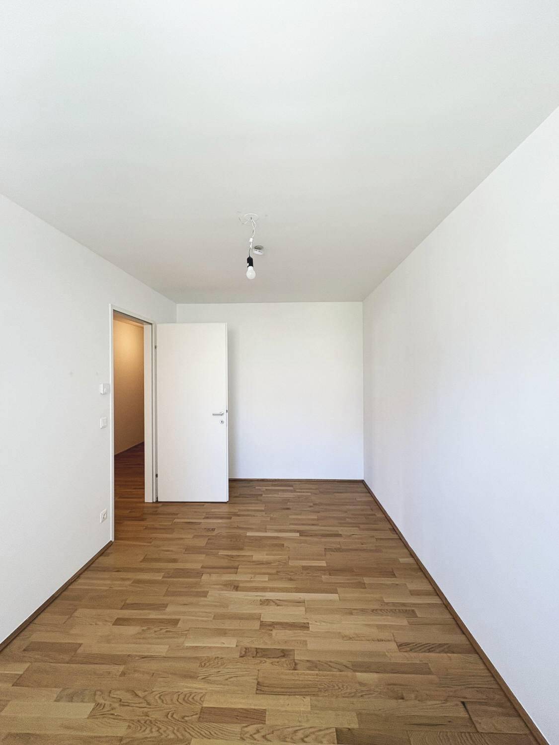 Geräumiges Zimmer mit Holzboden und weißen Wänden, ideal als Schlaf- oder Arbeitszimmer.