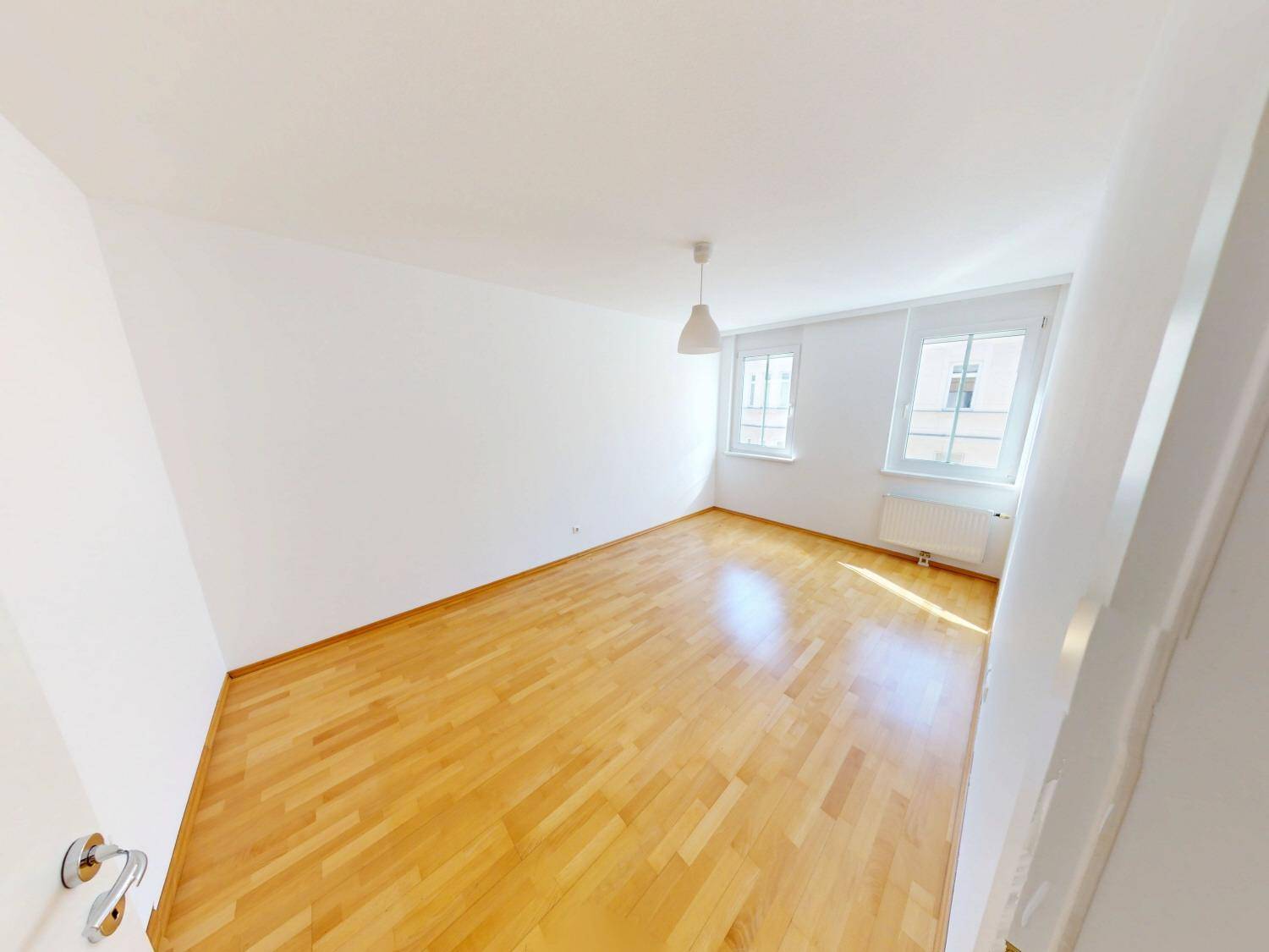 Geräumiges Schlafzimmer mit hellem Parkettboden und zwei Fenstern für viel Tageslicht.