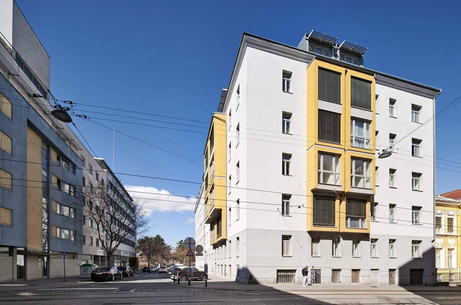 Modernes Wohnhaus mit gelben Akzenten und großen Fenstern an einer belebten Straße.