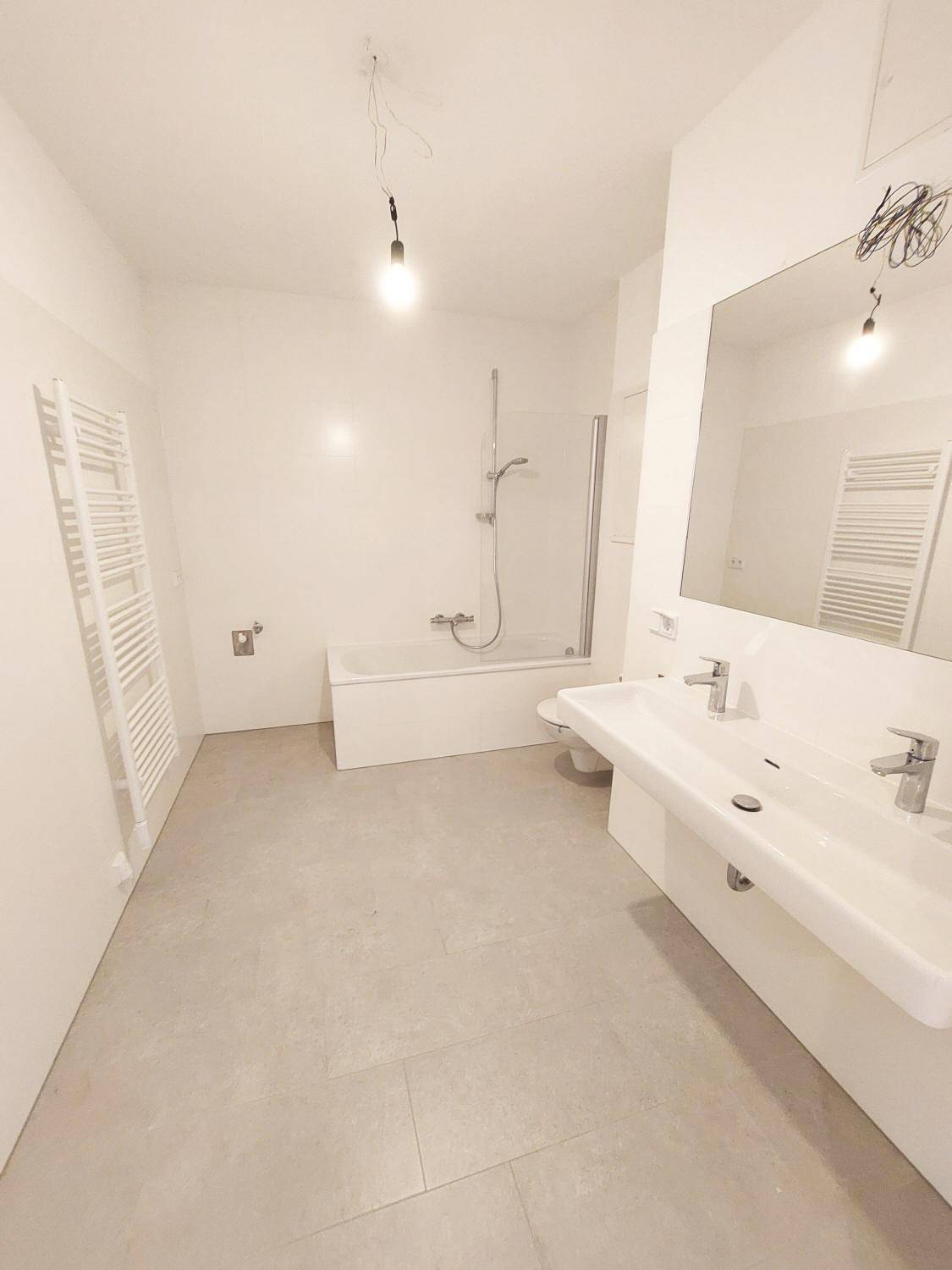 Helles Badezimmer mit Doppelwaschbecken, Badewanne und beheiztem Handtuchhalter.