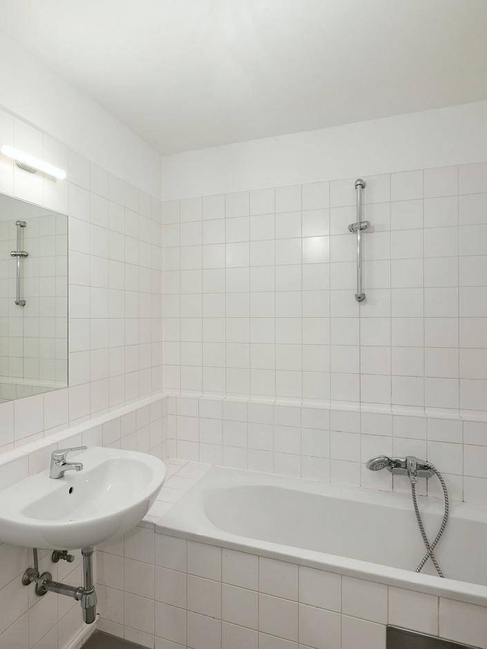 Helles Badezimmer mit weißen Fliesen, einer Badewanne und einem einzelnen Waschbecken.