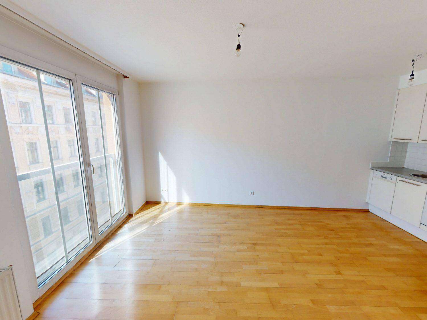 Wohnbereich mit Parkettboden, großen Fenstern und integrierter Küchenzeile.