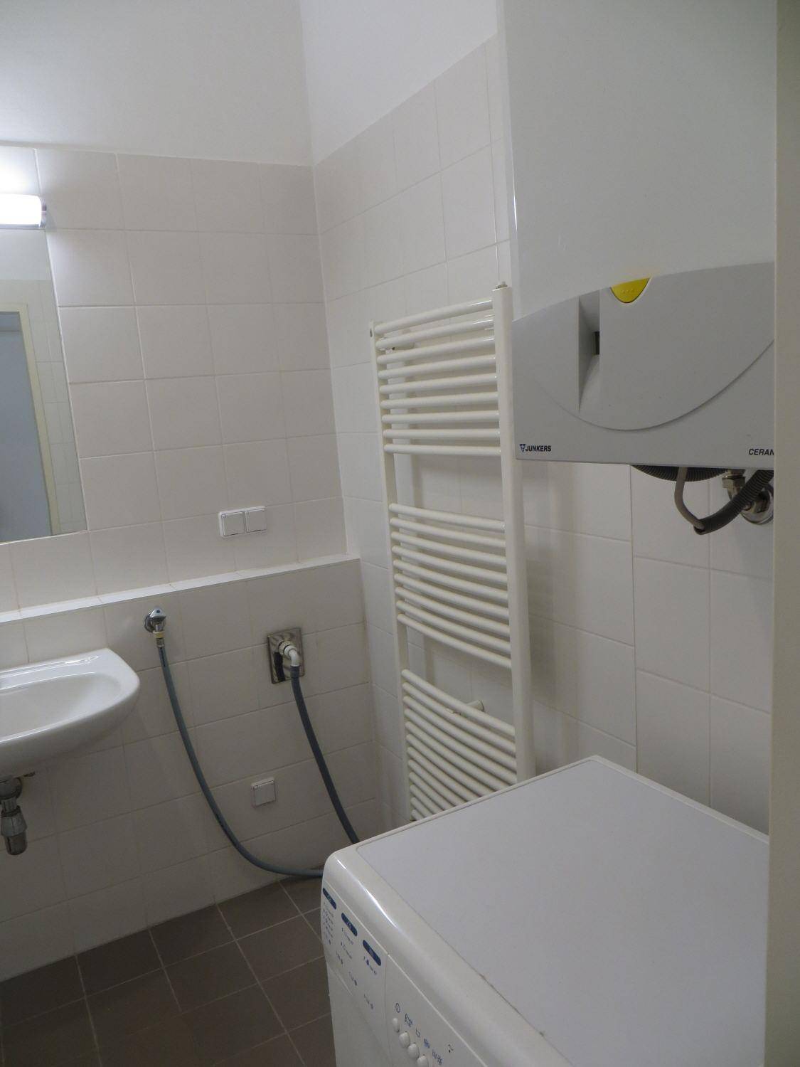 Gefliestes Badezimmer mit Waschbecken, Handtuchheizkörper und Waschmaschinenanschluss.