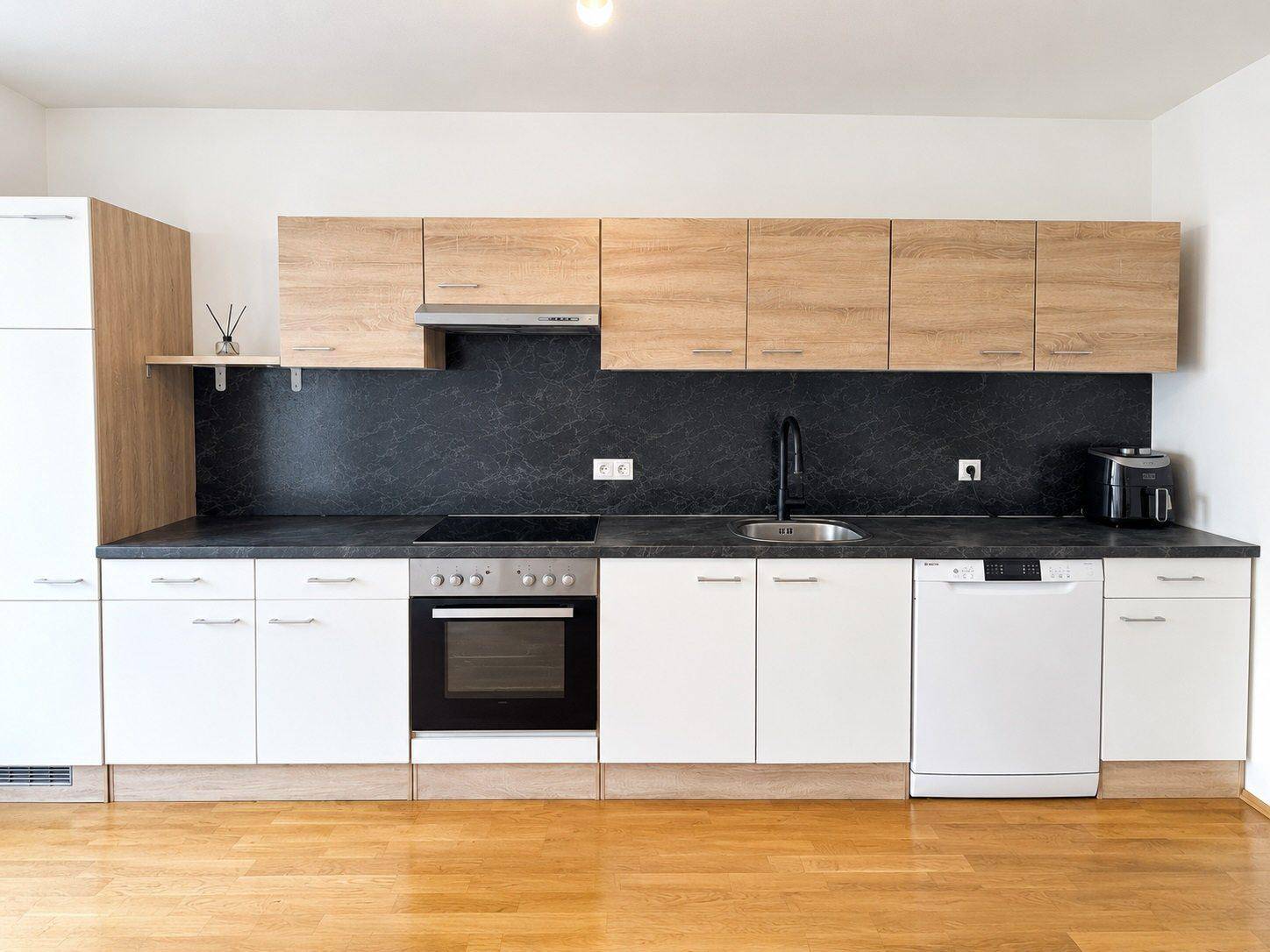 Moderne Einbauküche mit hellen Holz- und weißen Fronten, ausgestattet mit Backofen und Geschirrspüler.