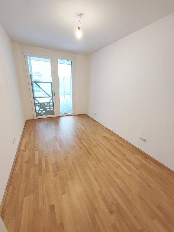 Helles Zimmer mit Holzboden und Zugang zu einem Außenbereich.