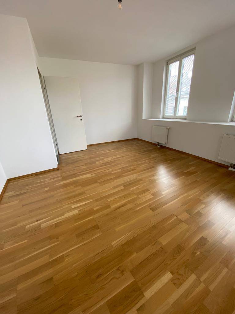 Helles, leeres Zimmer mit Parkettboden und zwei Fenstern, ideal als Schlaf- oder Arbeitszimmer.