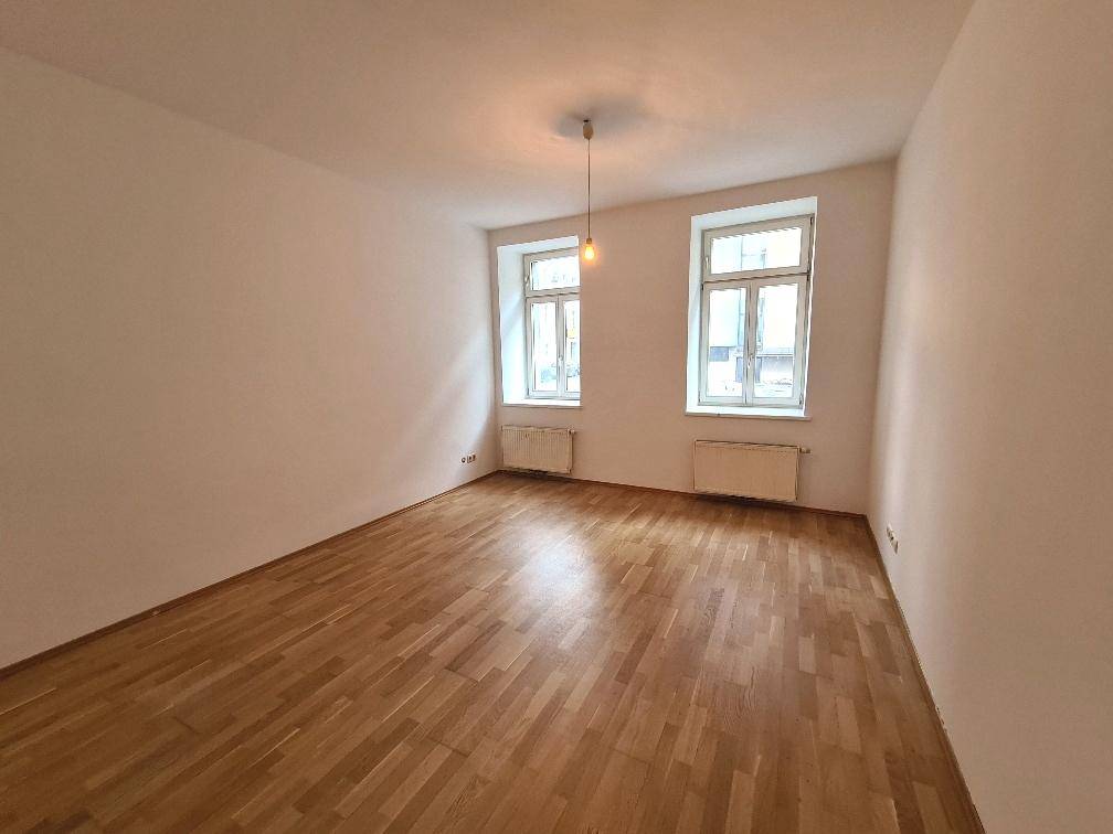 Heller Raum mit klassischem Parkettboden und zwei großen Fenstern, ideal als Wohn- oder Schlafzimmer.