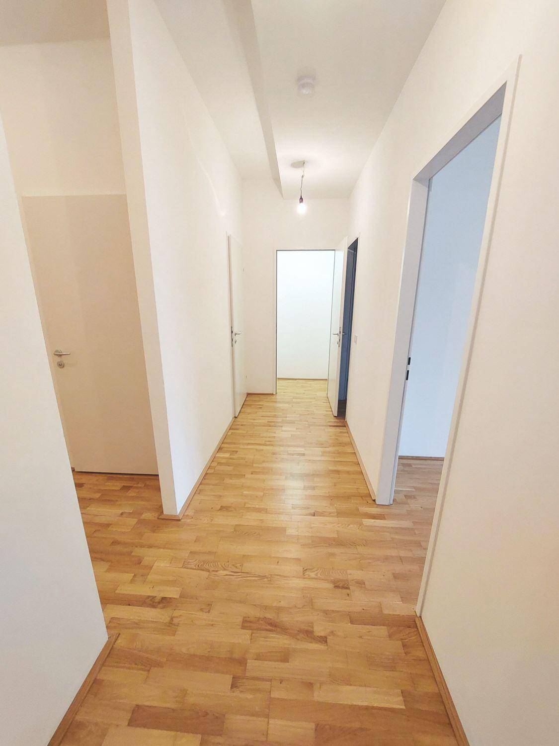 Heller Flur mit Parkettboden, weißen Wänden und mehreren Türen zu den angrenzenden Räumen.
