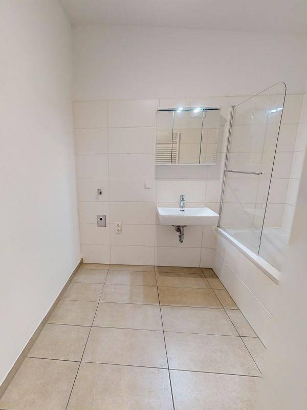 Modernes Badezimmer mit Badewanne, Duschabtrennung und hellen Fliesen.