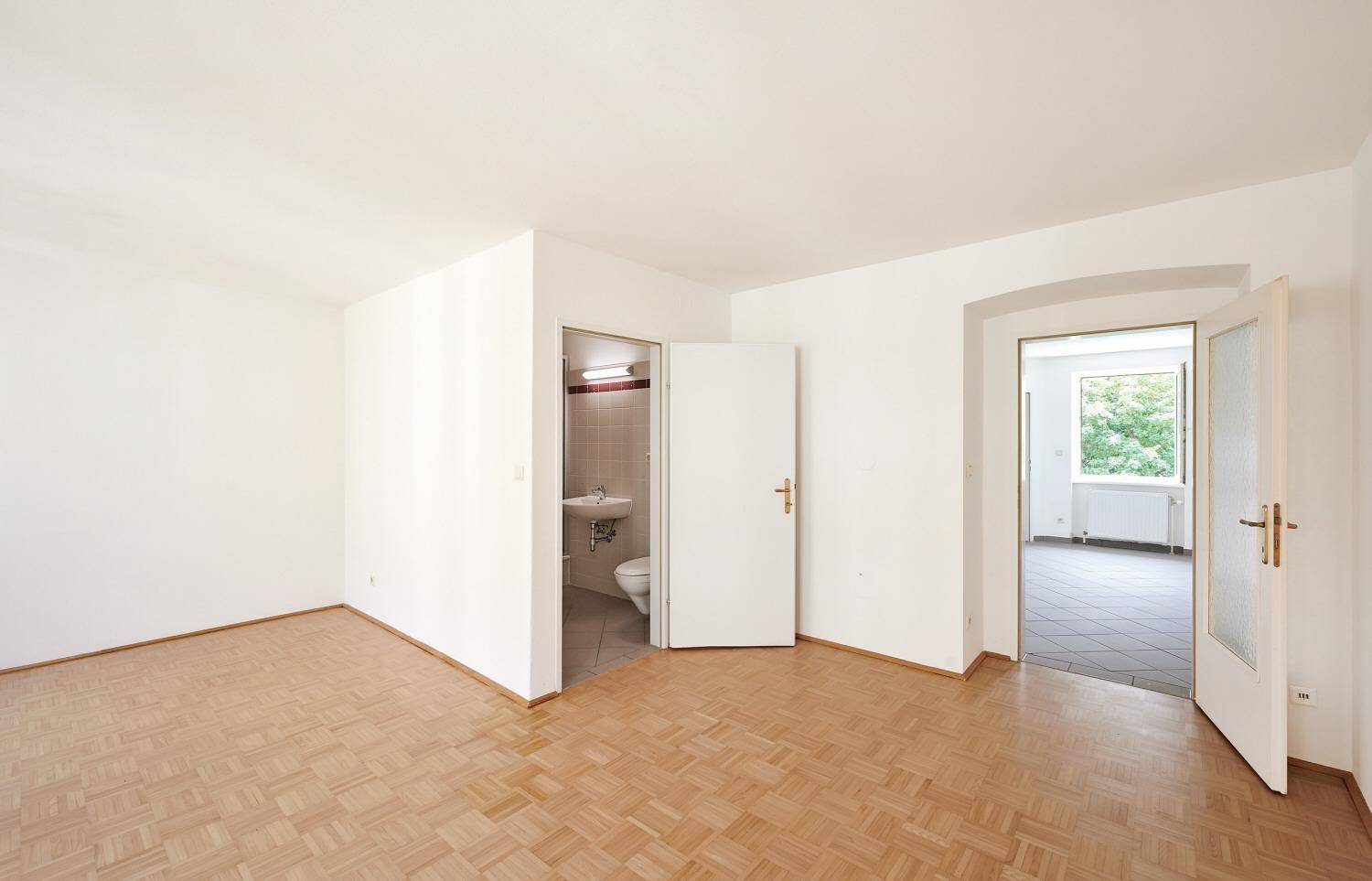 Heller Wohnraum mit Parkettboden und direktem Zugang zu einem kleinen Badezimmer mit WC.