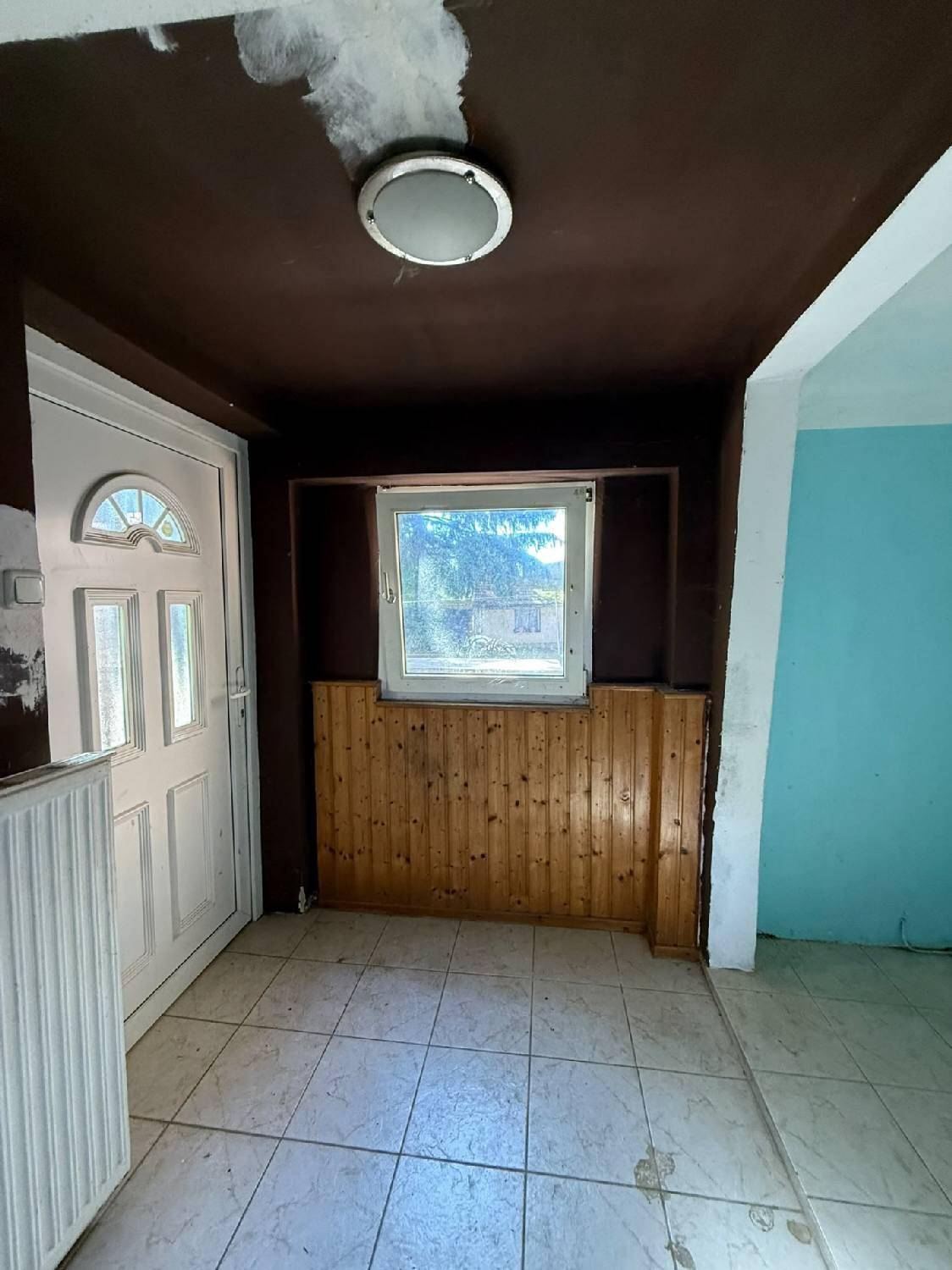 Eingangsbereich mit Fliesenboden, Holztäfelung und einer weißen Eingangstür.