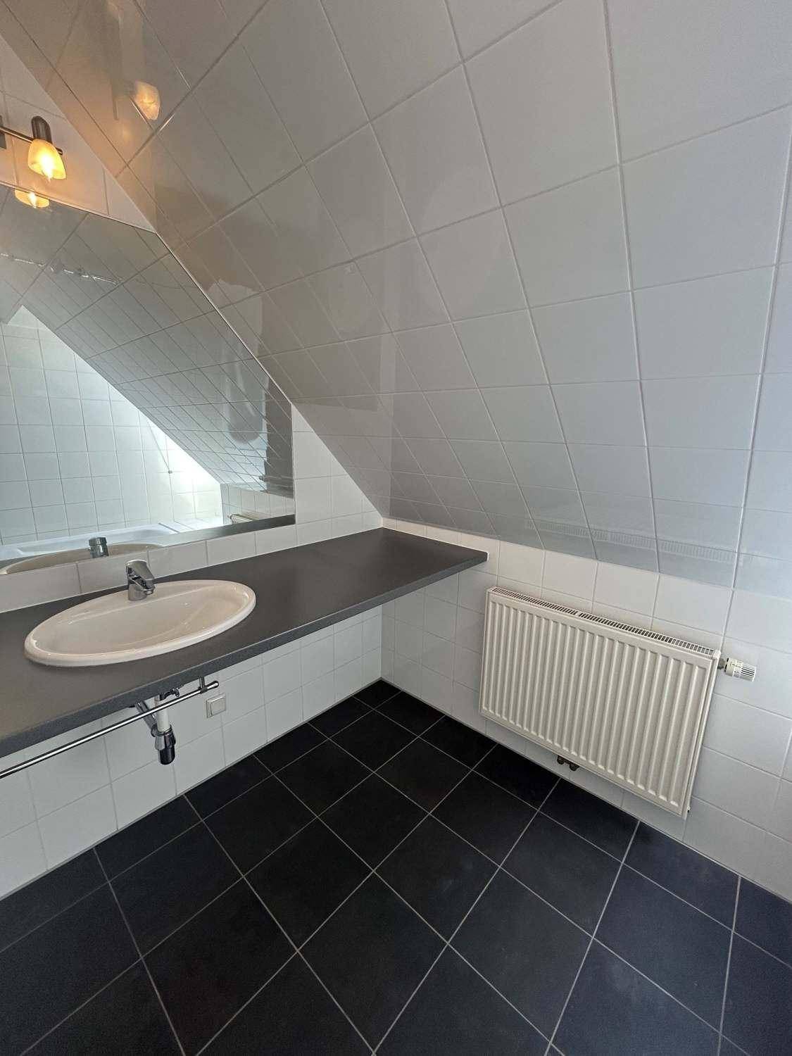 Badezimmer mit Einzelwaschbecken, Spiegel, dunkler Arbeitsplatte und Fliesenboden.