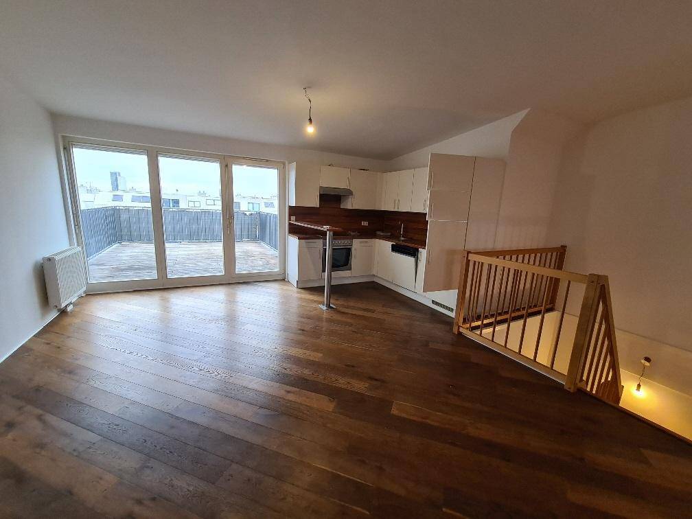 Offener Wohnbereich mit Holzboden, integrierter Küche und Zugang zu einer großen Terrasse.